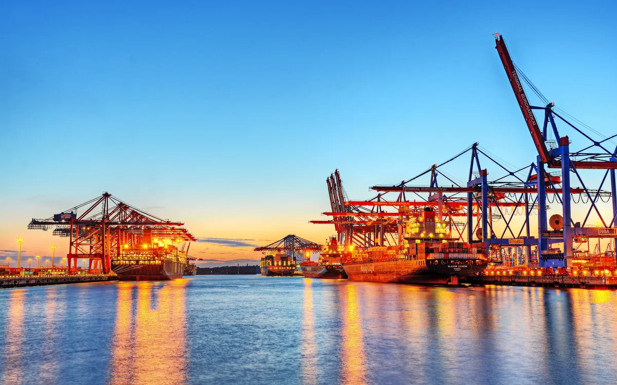 Hafen bei Sonnenuntergang mit Kränen und beleuchteten Frachtschiffen.