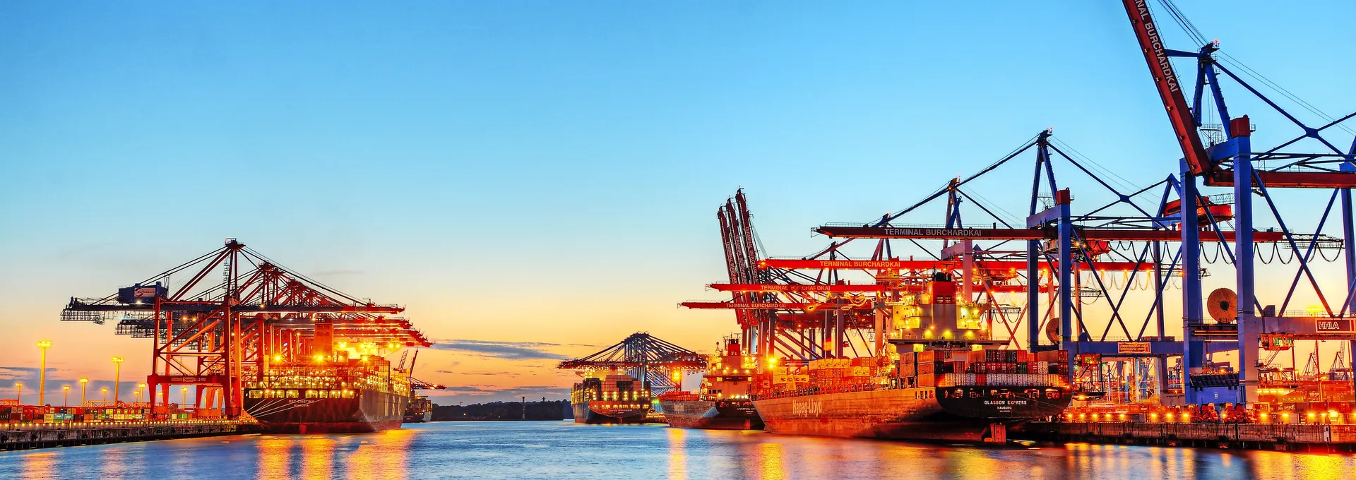 © Marco2811 - Fotolia Hafen bei Sonnenuntergang mit Kränen und beleuchteten Frachtschiffen.