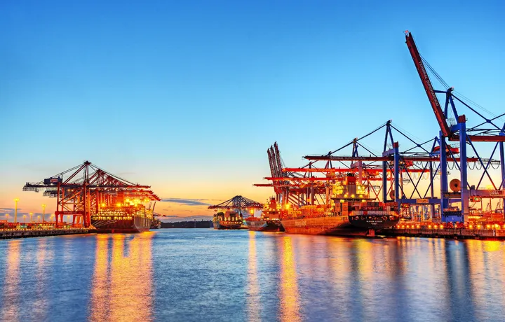 Hafen bei Sonnenuntergang mit Kränen und beleuchteten Frachtschiffen.
