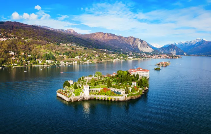 Luftaufnahme einer Insel mit historischem Gebäude in einem See umgeben von Bergen.