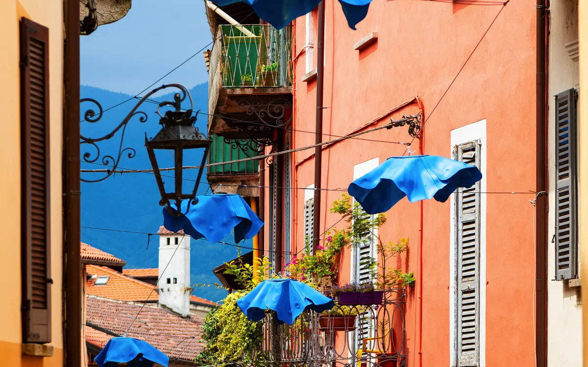 Gasse mit bunten Gebäuden und blauen Regenschirmen über der Straße