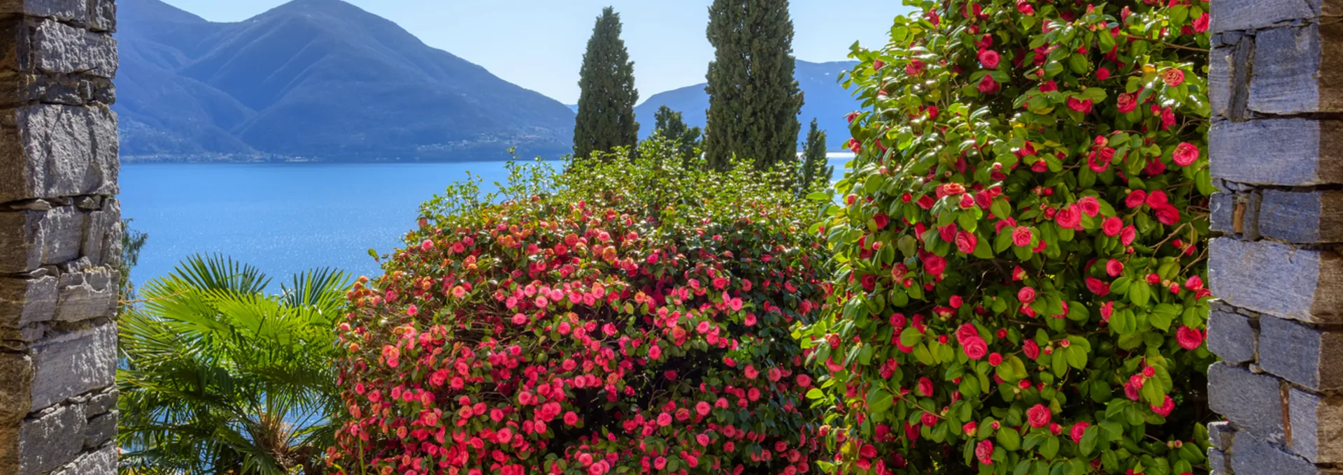 © Boris Stroujko - stock.adobe.com Blick durch einen Steinbogen auf See und blühende Büsche im Garten.