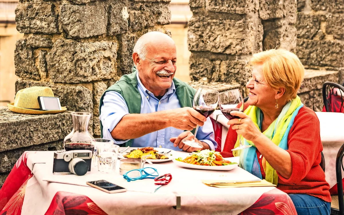Älteres Paar stößt bei einem Essen im Freien mit Rotwein an.