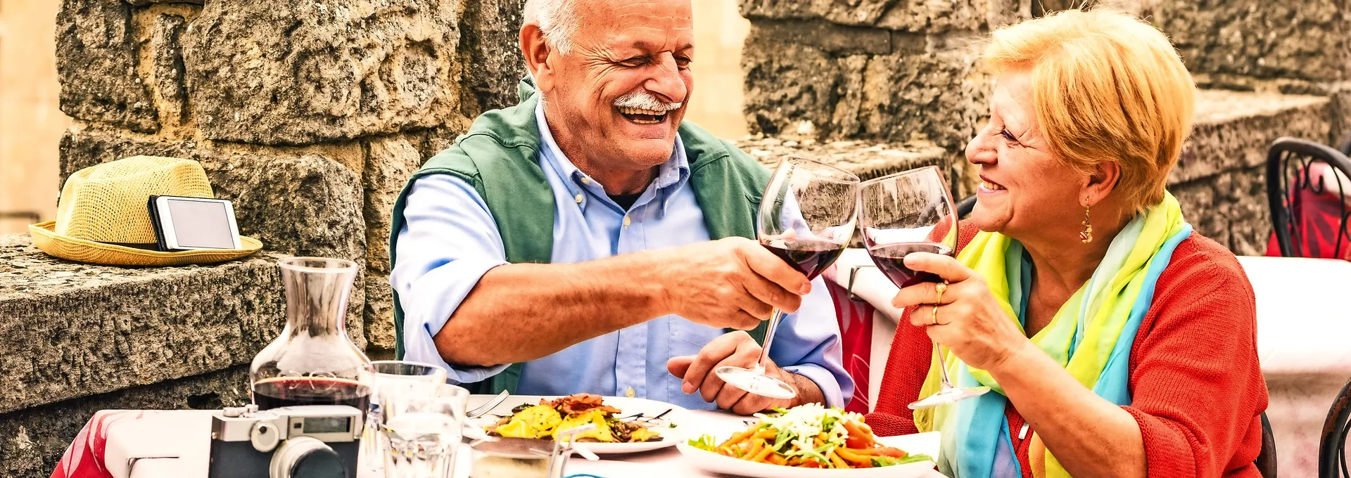 Älteres Paar stößt bei einem Essen im Freien mit Rotwein an.