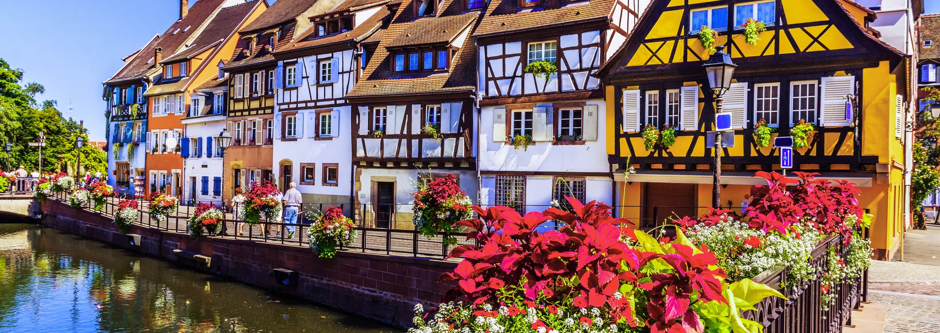 Fachwerkhäuser an einem Kanal mit Blumen geschmückter Brücke.