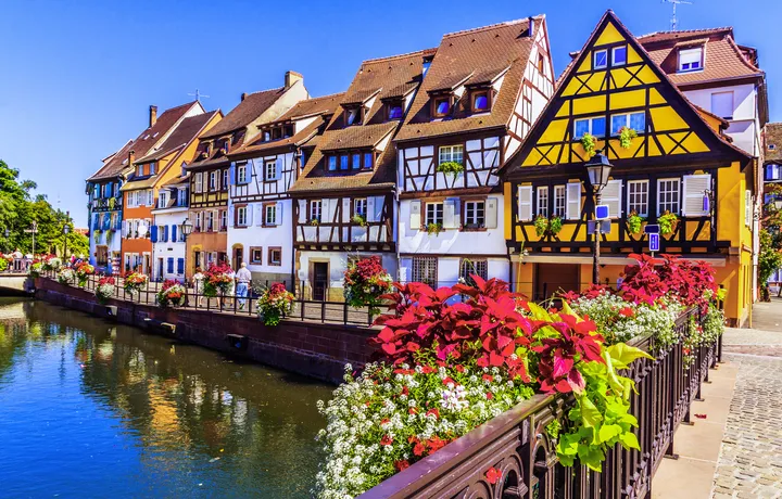 Fachwerkhäuser an einem Kanal mit Blumen geschmückter Brücke.