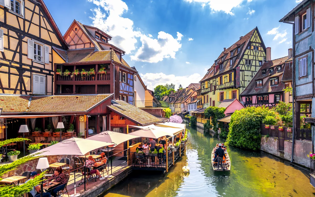 Fachwerkhäuser an einem Kanal mit Boot und Touristen in einer malerischen Altstadt.