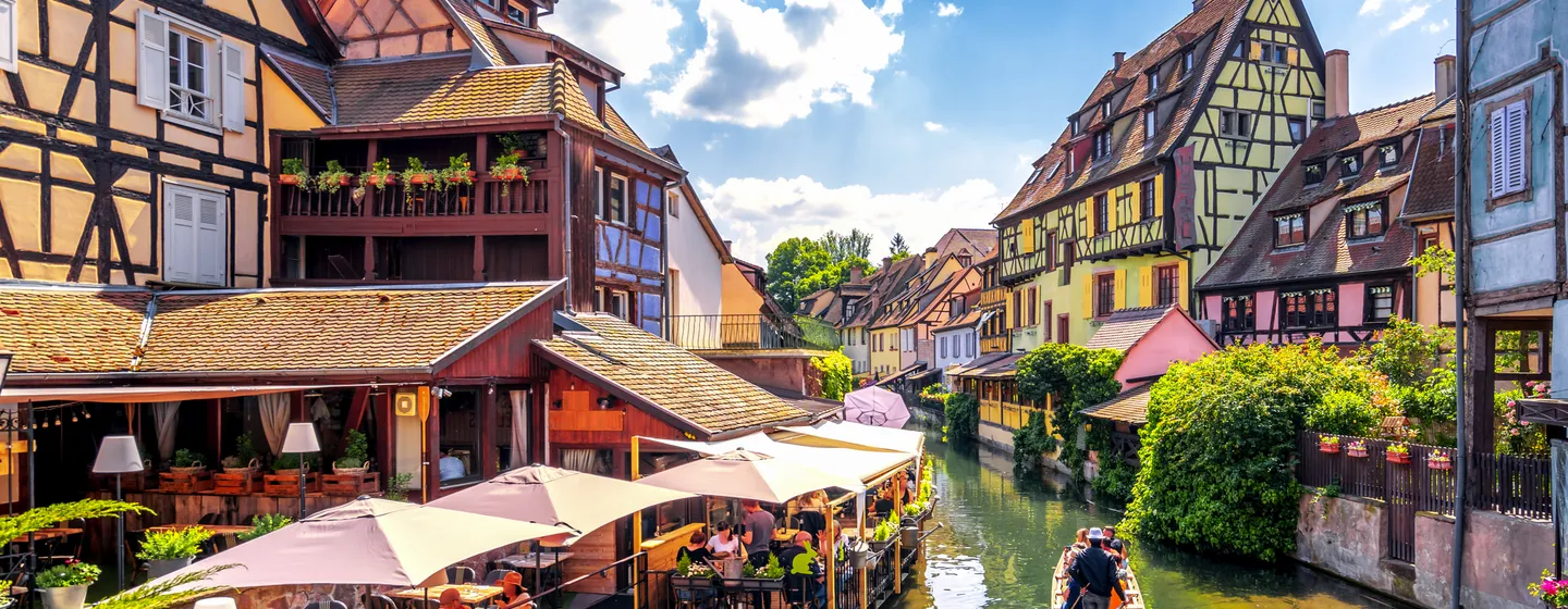 Fachwerkhäuser an einem Kanal mit Boot und Touristen in einer malerischen Altstadt.