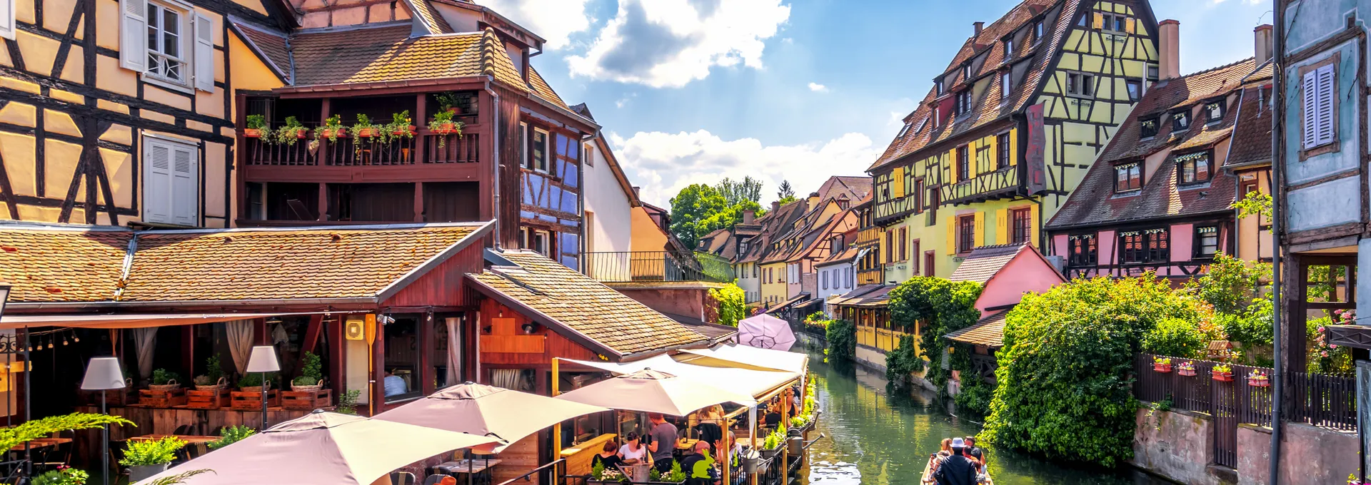 Fachwerkhäuser an einem Kanal mit Boot und Touristen in einer malerischen Altstadt.