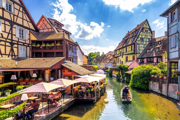 Fachwerkhäuser an einem Kanal mit Boot und Touristen in einer malerischen Altstadt.