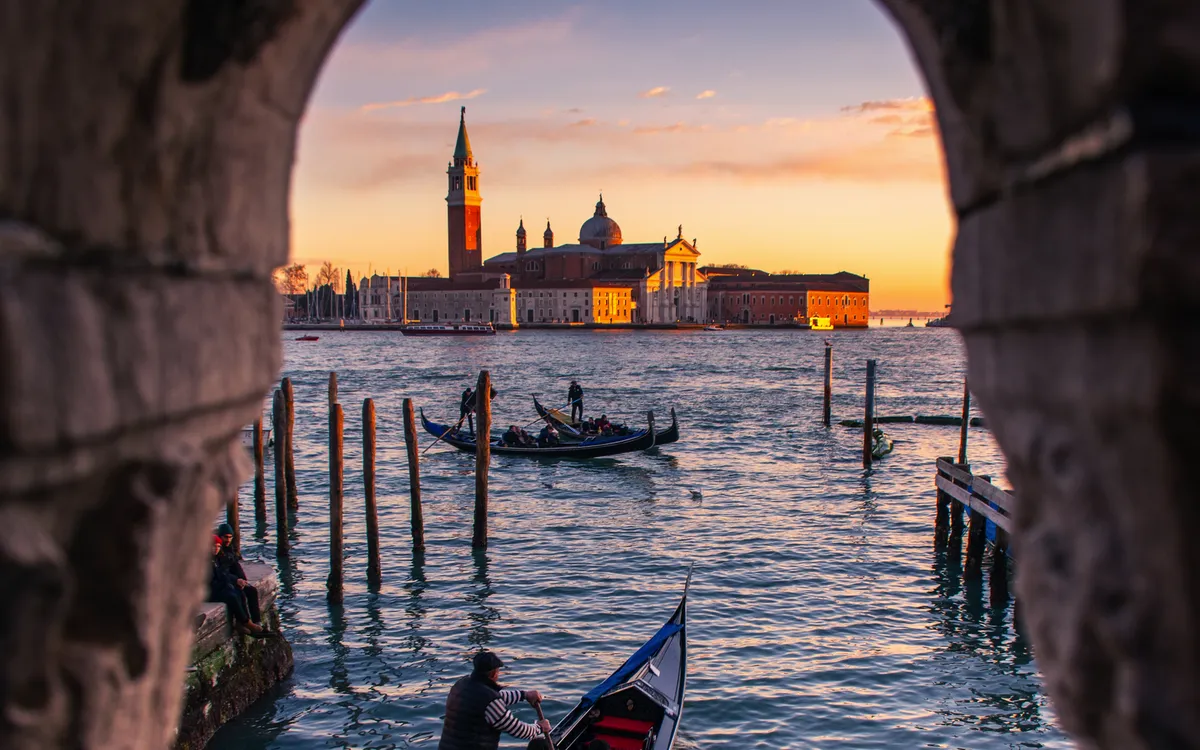 Gondeln auf dem Wasser mit Blick auf venezianische Insel bei Sonnenuntergang.