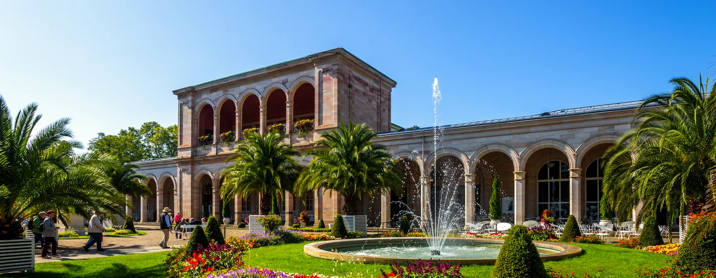 Historisches Gebäude mit Arkaden, Brunnen und Garten.