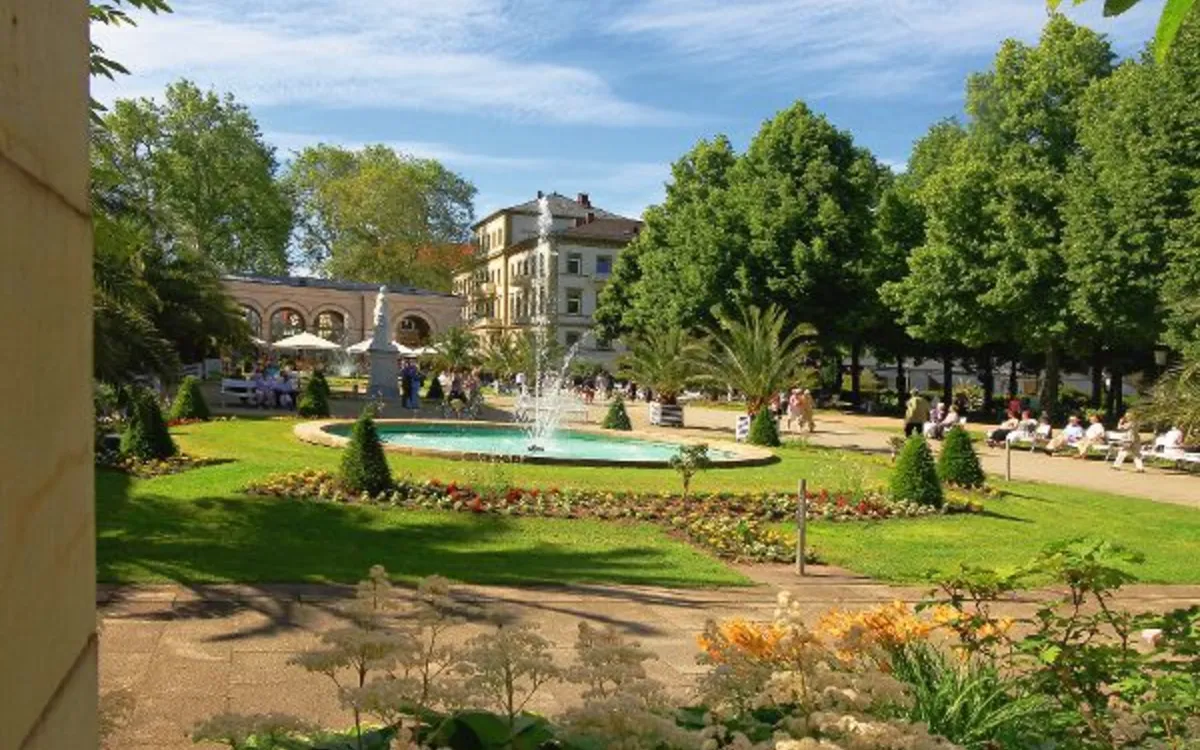 Springbrunnen im Kurgarten von Bad Kissingen, umgeben von Blumen und Bäumen.