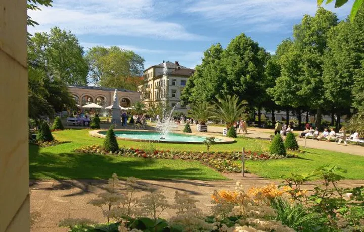 Springbrunnen im Kurgarten von Bad Kissingen, umgeben von Blumen und Bäumen.