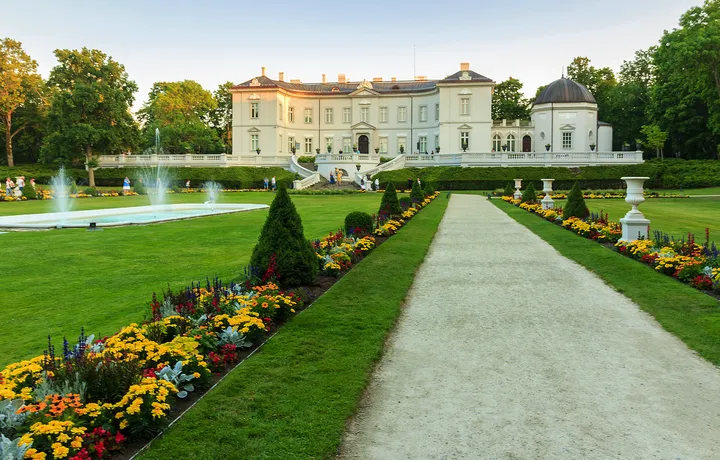Weg zu einem Schloss mit Gärten und Springbrunnen im Vordergrund.